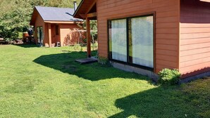 Une cabane en bois dotée d’une grande fenêtre, d’un porche abrité et d’une pelouse bien entretenue.