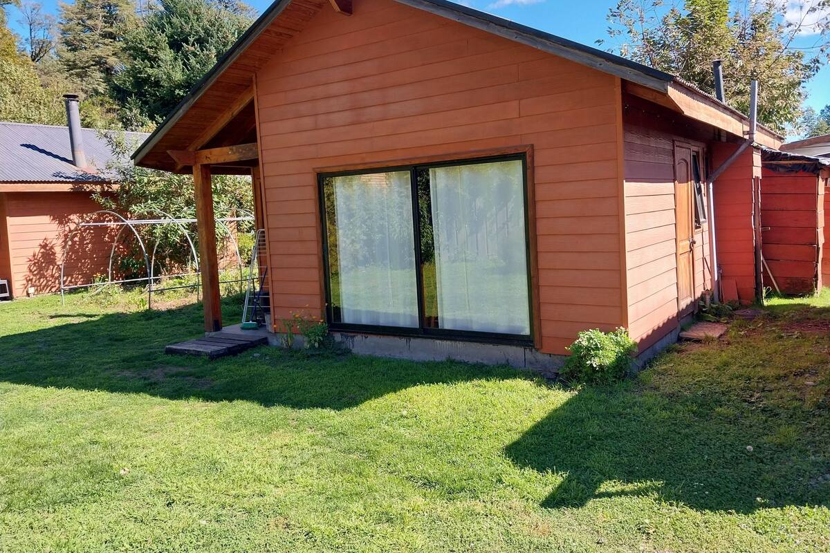 Ein einstöckiges Holzhaus mit einem großen Schiebeglastür, einer überdachten Veranda und einem kleinen Garten.