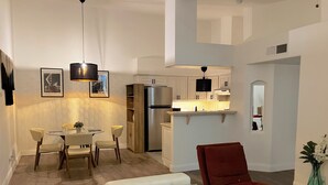A modern living room with a white sofa, a red armchair, and a dining area with a table and chairs. There is a kitchen with white cabinets and a refrigerator. - Contemporary luxurious Condo with Mountain View’s in Henderson . WiFi, Roku TV.  (Henderson)