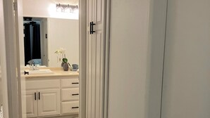A hallway with a bathroom featuring a vanity, mirror, and a plant. - Contemporary luxurious Condo with Mountain View’s in Henderson . WiFi, Roku TV.  (Henderson)