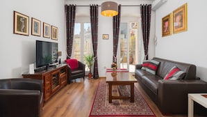 Una sala de estar con un sofá, un televisor, un mueble de madera, un tapete rojo y una planta en maceta.
