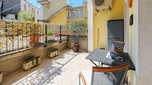 Un pequeño patio con una mesa y sillas, plantas en macetas y vistas a edificios vecinos.