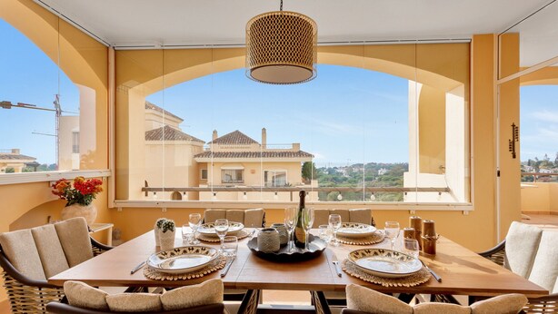 A dining area with a table set for four, a hanging light fixture, and a view of a building through large windows. - Charming Villa With Terrace (Marbella)