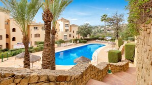 A swimming pool surrounded by stone walls, palm trees, and a building with multiple balconies. - Charming Villa With Terrace (Marbella)