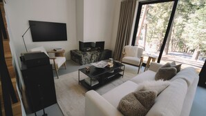 Una sala de estar moderna con un televisor de pantalla plana grande, un sofá, una mesa de centro y una silla.