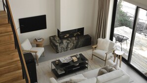 Una sala de estar moderna con un sofá blanco, una mesa de centro, un televisor montado en la pared y un ventanal con cortinas.