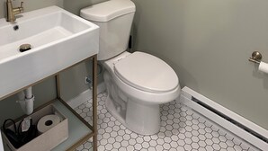 A bathroom with a white sink, toilet, and a towel hanging on a towel ring. - The Innwoods - Studio Apartment 1 (Tannersville)
