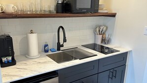 A modern kitchen with a stainless steel dishwasher, a double sink, a microwave, and a wooden countertop. - The Innwoods - Studio Apartment 1 (Tannersville)