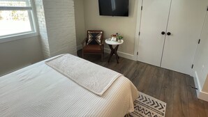 A bedroom with a bed, a chair, a small table with a plant, a TV on the wall, and a wardrobe. - The Innwoods - Studio Apartment 1 (Tannersville)