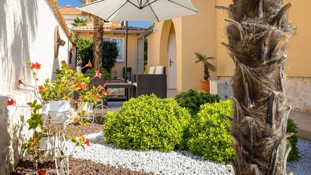 A courtyard with a white umbrella, a table with chairs, and a variety of plants and trees. - Apartment in Porec Near the Sea and Beaches (Porec)