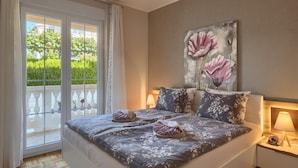 A bedroom with a bed, two bedside lamps, a large floral painting on the wall, and a view of greenery through a sliding door. - Apartment in Porec Near the Sea and Beaches (Porec)
