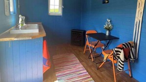 A room with a wooden ceiling, a blue wall, a small window, a wooden table, a chair, a rug, and a small plant. - Shepherds Hut in Dark Sky Reserve

 (Gwynfe)