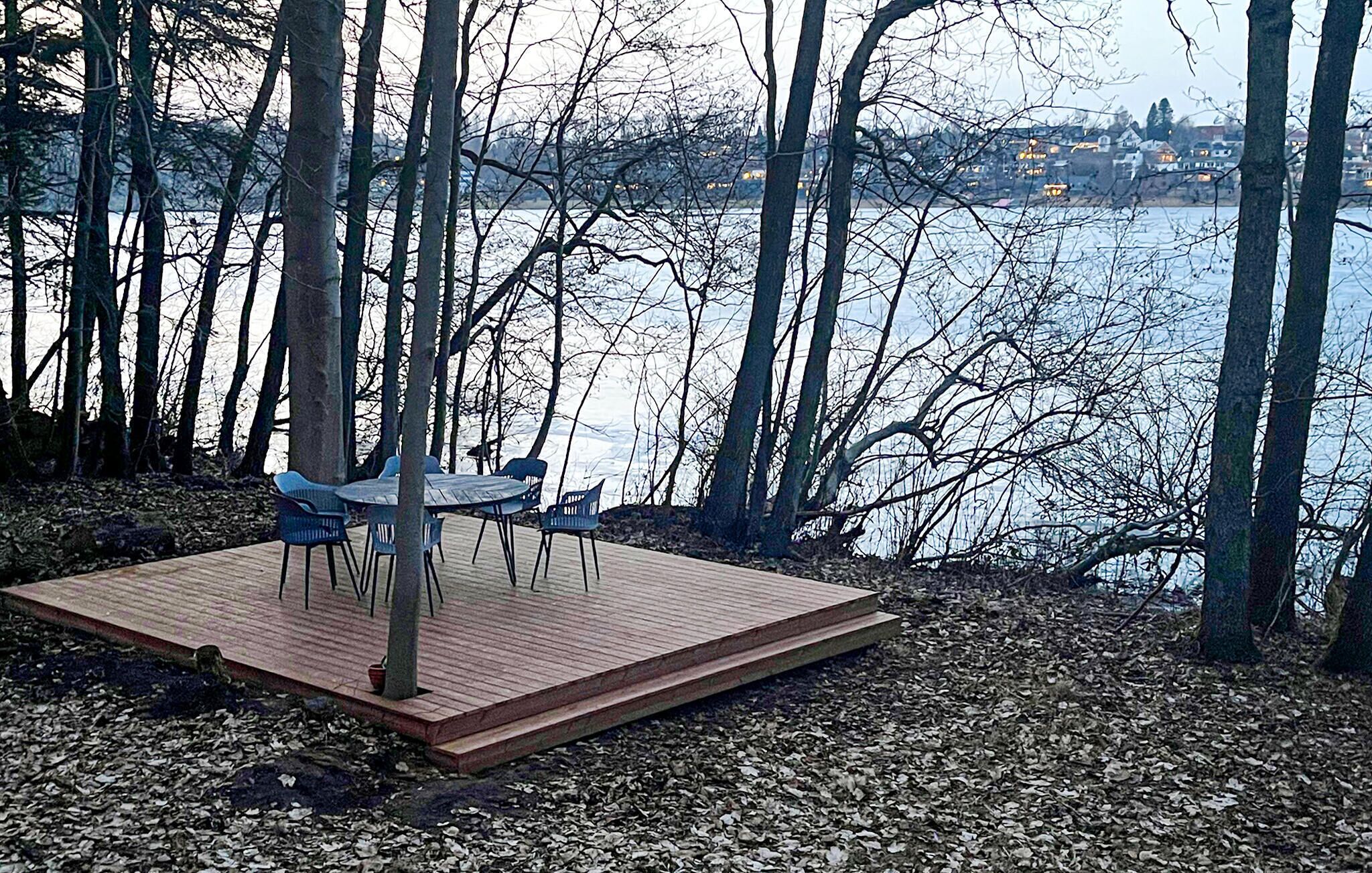 A wooden deck with chairs and a table, surrounded by trees and a body of water.