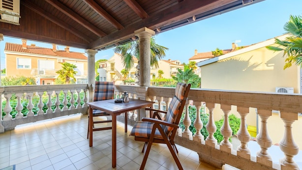 A covered outdoor seating area with a table and chairs, a balustrade, and a view of surrounding buildings. - Pretty Apartment With Balcony (Porec)