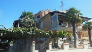 A multi-story house with balconies, a gated entrance, and palm trees. - Pretty Apartment With Balcony (Porec)