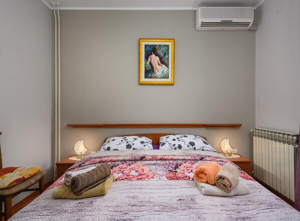 A neatly made bed with floral bedding, two bedside lamps, and a framed painting on the wall. - Pretty Apartment With Balcony (Porec)