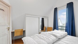 A bedroom with a bed, a mirror, a wicker chair, and a window with curtains. - 2 bedroom stunning home in Fanø (Fanø)