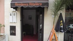 The entrance of a hotel with a red carpet leading inside. There is a black awning with the hotel's name above the door. - Coqueto apartment ghiliz (Marrakech)