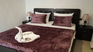 A double bed with a dark patterned bedspread and two pillows, a bedside table with a lamp, and a nightstand with a lamp. - Coqueto apartment ghiliz (Marrakech)