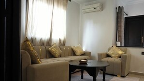 A living room with a sofa and armchair, a coffee table, and a flat-screen TV mounted on the wall. - Coqueto apartment ghiliz (Marrakech)