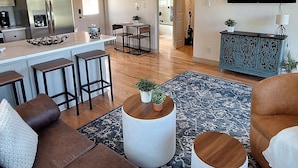 A spacious living area with a high ceiling, a kitchen with modern appliances, a dining area, and a staircase leading to an upper level. - Cozy Cabin by the Lake (Tyler)