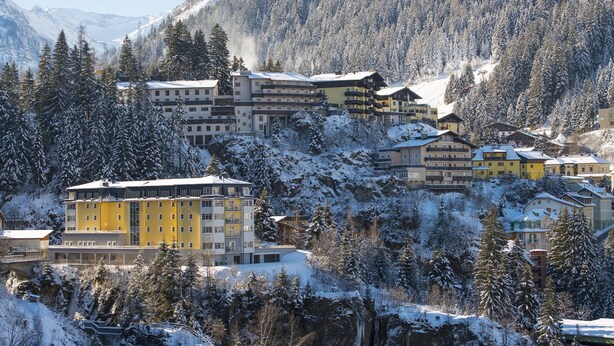 Une station de montagne enneigée, avec des bâtiments à plusieurs étages, un télésiège et une cascade.
