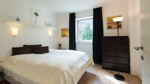 Une chambre à coucher avec un grand lit, une commode, une fenêtre avec des rideaux, des lampes fixées au mur et un tableau.