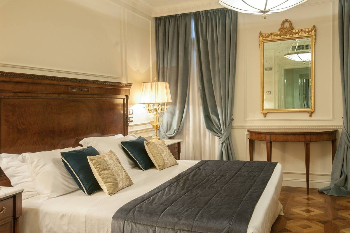 Una camera d'albergo con un letto grande, un comodino con una lampada, uno specchio e una piccola scrivania.