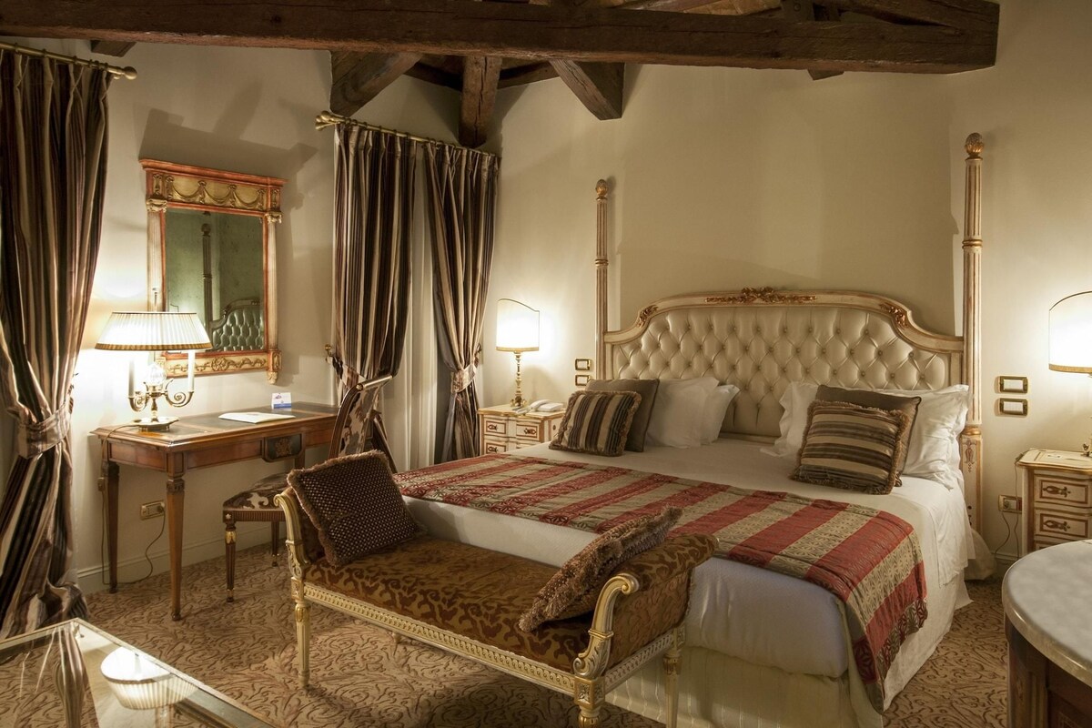 Un dormitorio clásico con una cama grande, cabecera ornamentada y un espejo sobre el tocador.