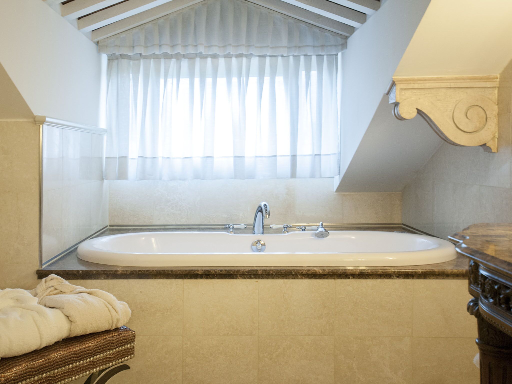 Une salle de bain avec une baignoire sur pieds, une fenêtre ornée de rideaux légers et un meuble-lavabo en bois.