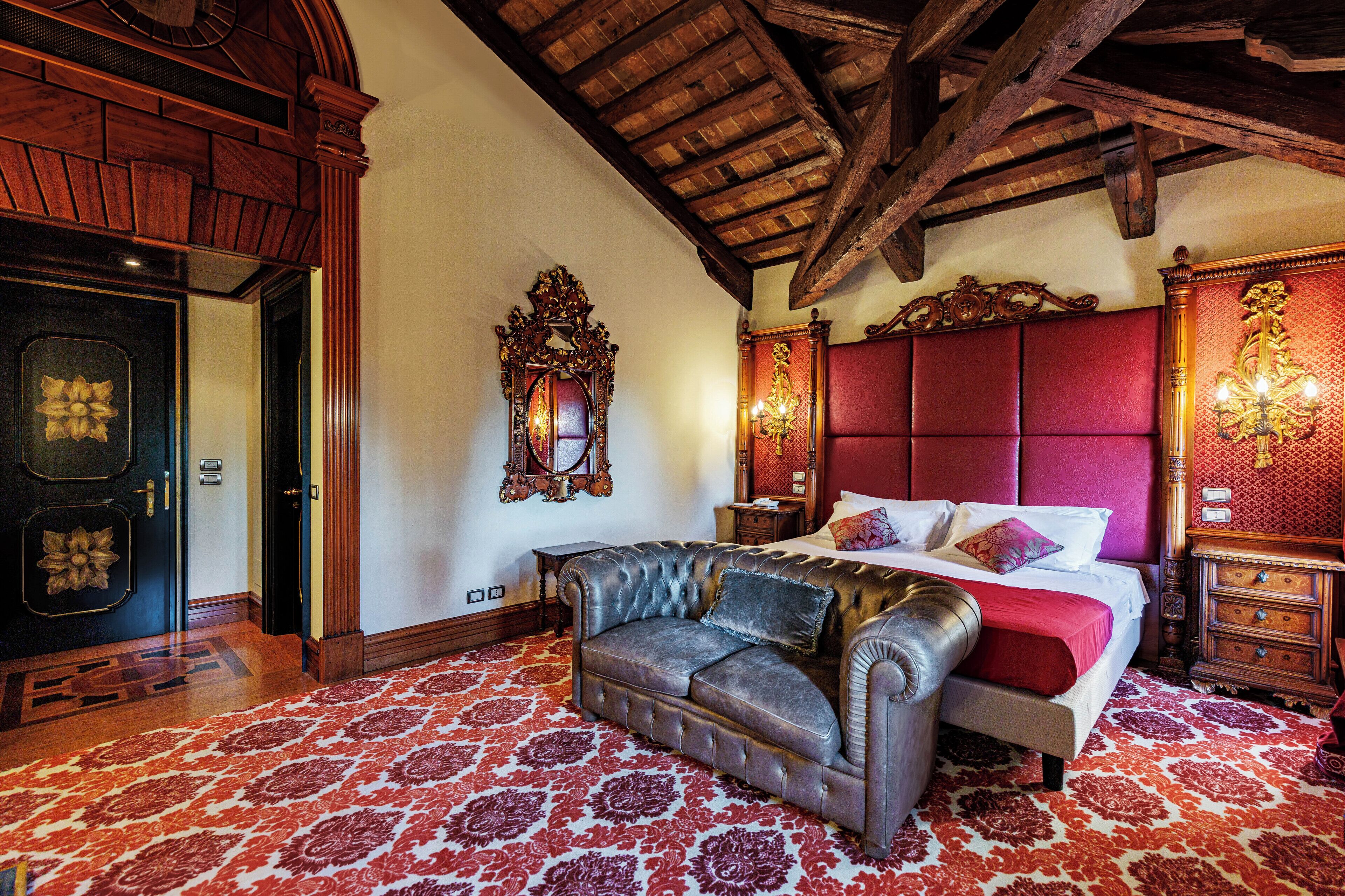 A bedroom with a large bed, a leather sofa, a wooden dresser, and a chandelier.