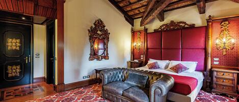 A bedroom with a large bed, a leather sofa, a wooden dresser, and a chandelier.