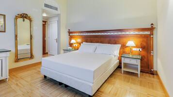 Un dormitorio ordenado con una cama grande, dos mesitas de noche con lámparas, un cabecero de madera, un espejo de cuerpo entero y piso de madera.