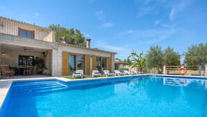A swimming pool with lounge chairs and a lifebuoy, surrounded by a stone building with large windows and a patio area. - 4 bedroom villa with private pool and barbecue (Inca)