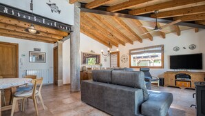 A spacious living area with a grey sofa, wooden beams, a dining table with chairs, a TV, and a fireplace. - 4 bedroom villa with private pool and barbecue (Inca)
