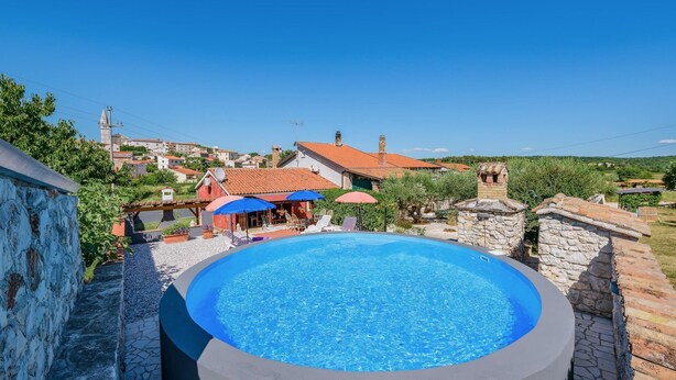 A swimming pool with a stone border, surrounded by a stone wall and a view of a village with buildings and a church in the background. - Nice Apartment With Pool (Visnjan)