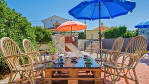 A wooden table with six wicker chairs, two umbrellas, and a stone wall in the background. - Nice Apartment With Pool (Visnjan)