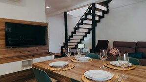 A dining area with a wooden table set for four, a TV mounted on the wall, and a staircase with black railings. - WELCS DUPLEX 192 PDA cerca del mar (Platja d´Aro)
