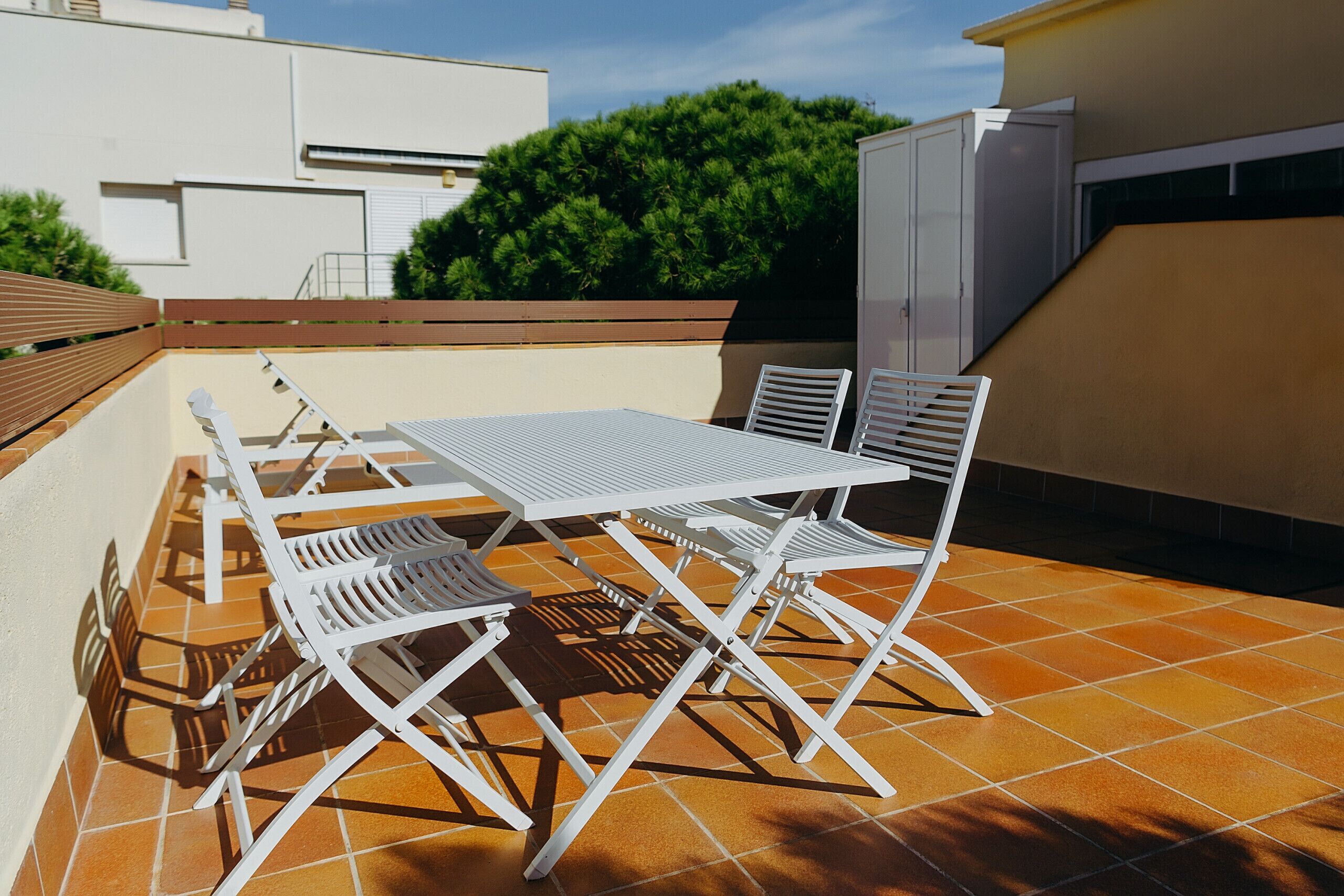 An outdoor patio with a white metal table and chairs, surrounded by orange-tiled flooring.