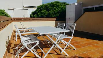 An outdoor patio with a white metal table and chairs, surrounded by orange-tiled flooring.
