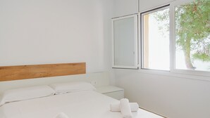 A bedroom with a wooden headboard, a bed with white linens, two nightstands, and a window with a view of a tree. - WELCS DUPLEX 192 PDA cerca del mar (Platja d´Aro)