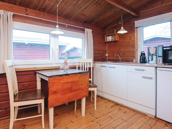 A cozy cabin-style kitchen with wooden walls, a wooden dining table, and a white sink. - 2 Person Holiday Park Home in Romo (Rømø)
