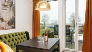 A modern living room with a green sofa, a dark wooden table, and a large window with orange curtains. - 2 Person Holiday Park Home in Romo (Rømø)