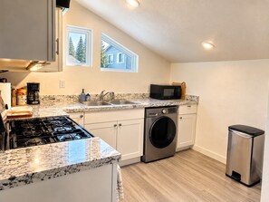 Cocina compacta con estufa a gas, microondas, pileta y lavadero integrado.