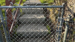 A residential property with a front yard, a wooden staircase leading to a front door, and a chain-link fence.