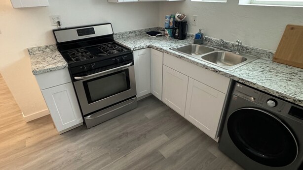 A compact kitchen with white cabinets, a built-in oven, a washing machine, and a granite countertop.