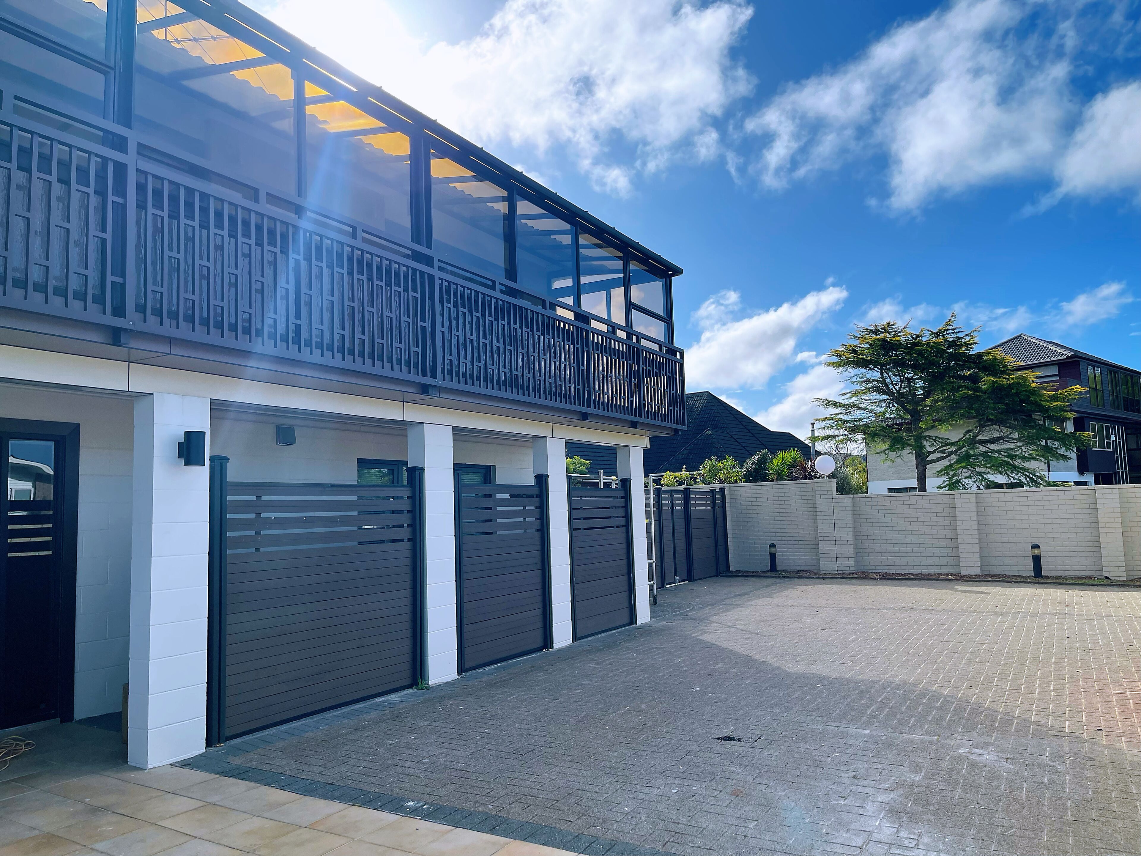 A modern two-story building with a balcony, garage doors, and a paved driveway.