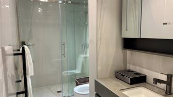 A modern bathroom with a glass-enclosed shower, a white sink, and a black vanity.
