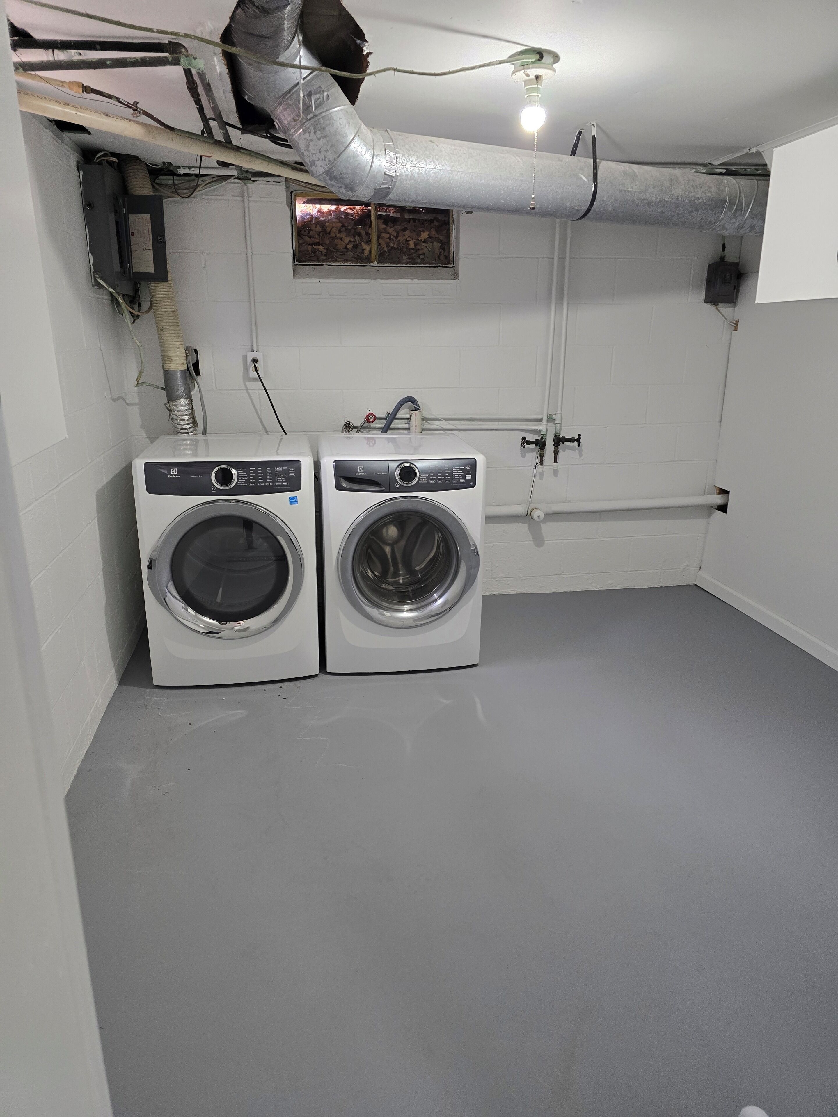 A laundry room with two front-loading washing machines, a small window, and a white tiled floor.