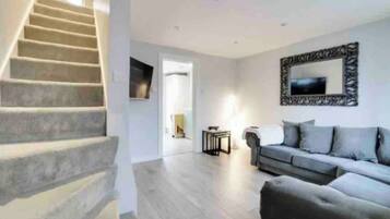 A staircase leading to a landing, a grey sofa, and a framed mirror on the wall.